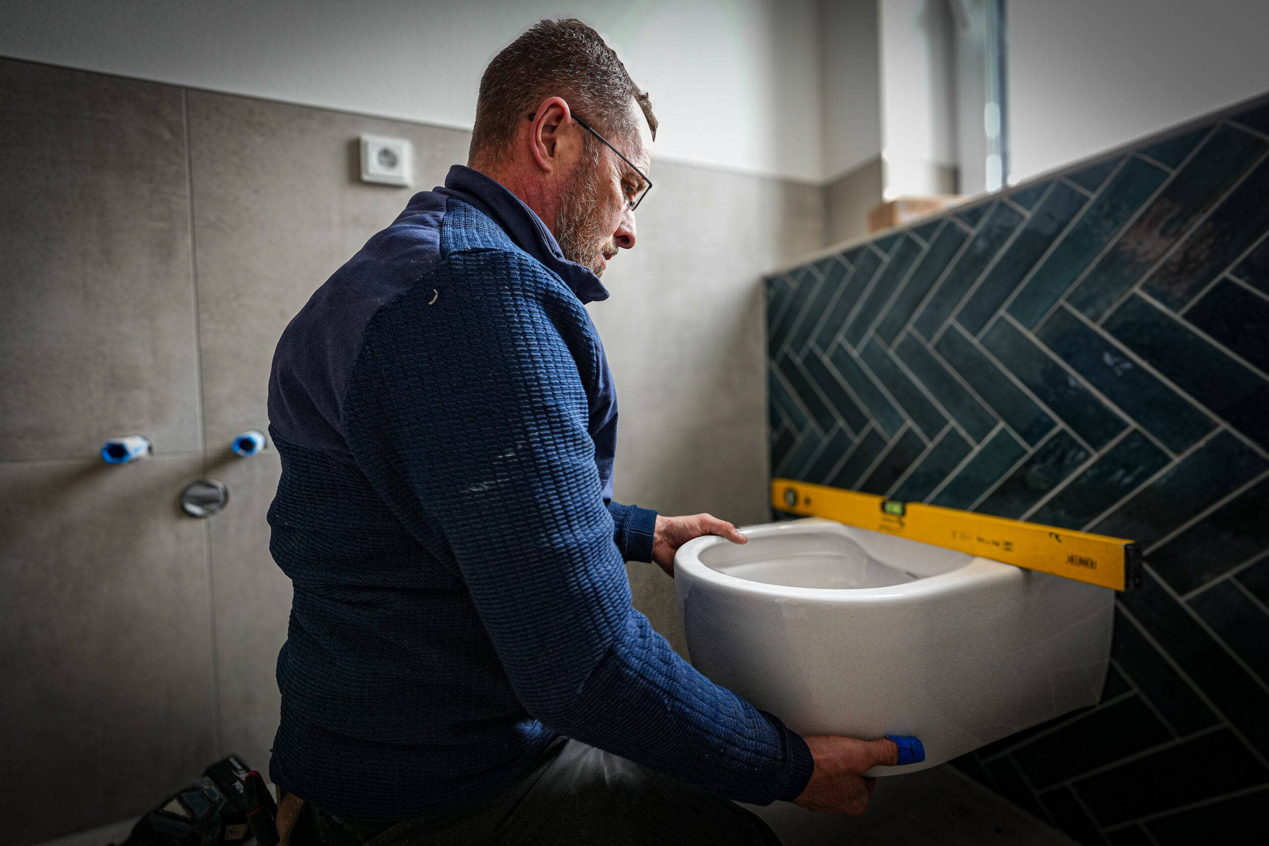 Monteur von Wolters Haustechnik beim Einbau eines wandhaengenden WCs in einem Badezimmer mit Wasserwaage