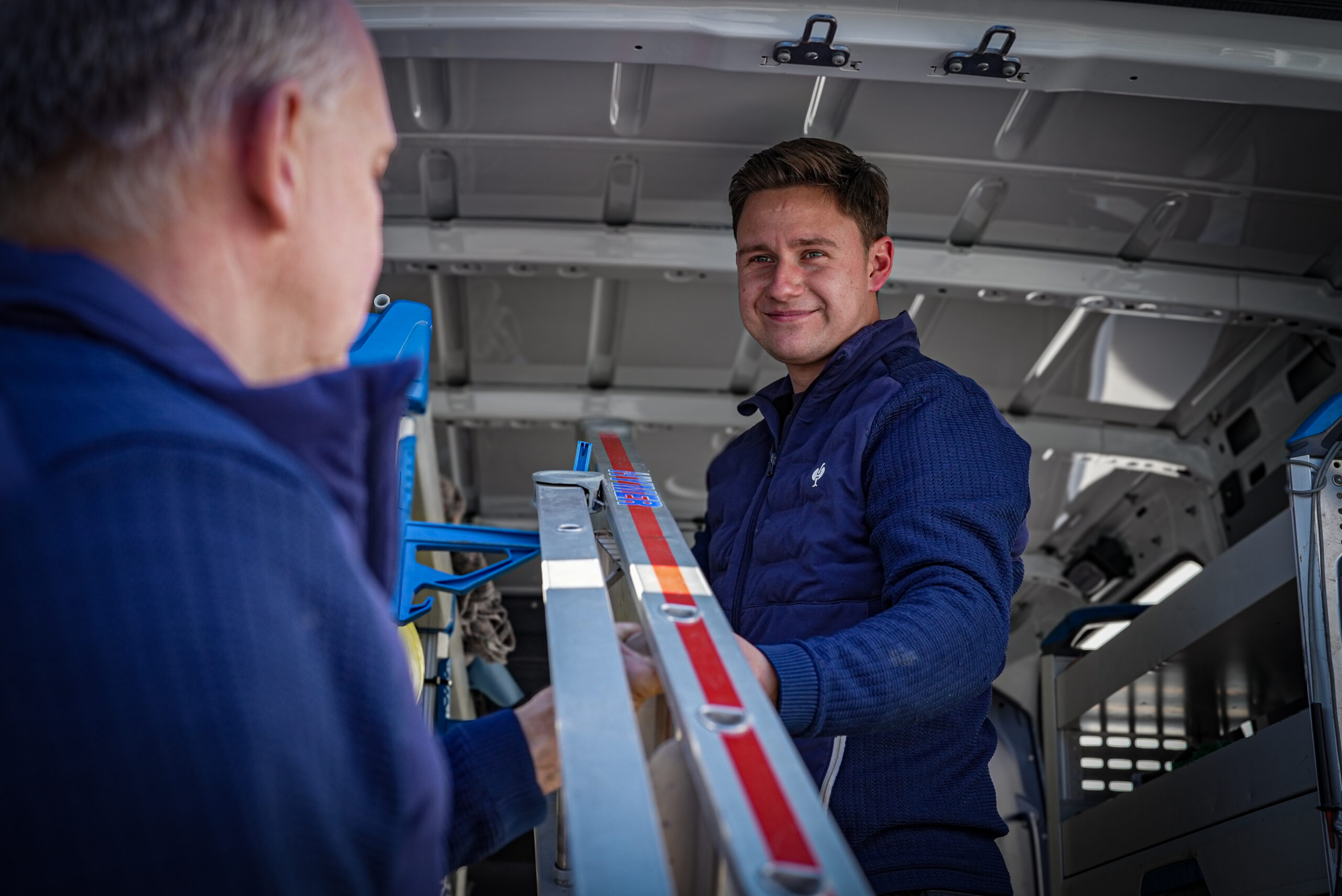 Zwei Monteure von Wolters Haustechnik entladen eine Leiter aus dem Firmentransporter